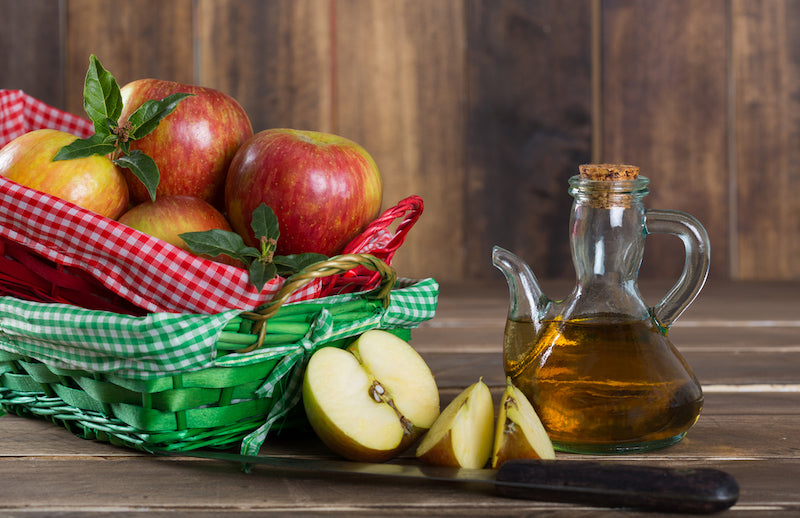 Jar of apple cider vinegar next to a basket of apples