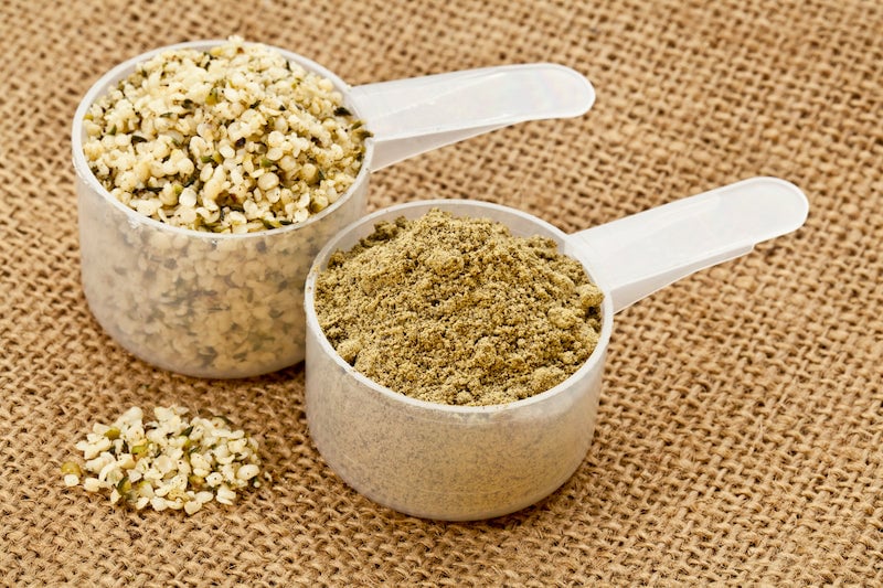 A scoop of hemp protein next to a scoop of hemp seeds