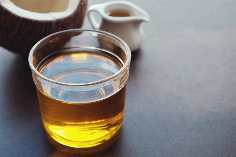 MCT oil in a clear glass, with half a coconut in the background