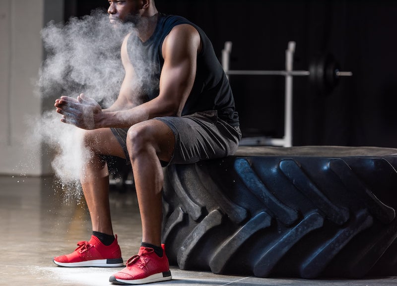 Hombre sentado sobre un neumático grande en un gimnasio, con polvo de tiza en el aire mientras aplaude