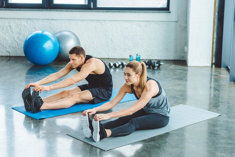 Man and woman stretching on gym mats in a gym setting