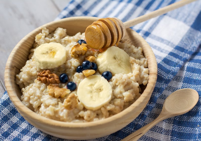 Protein oatmeal in a wooden bowl, topped with honey, nuts, and banana slices