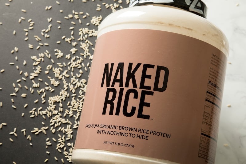 Imagen del producto Naked Rice con el producto de lado y granos de arroz esparcidos a su lado