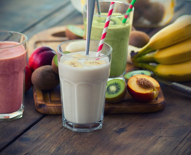 Tres batidos diferentes rodeados de varias frutas sobre una mesa.