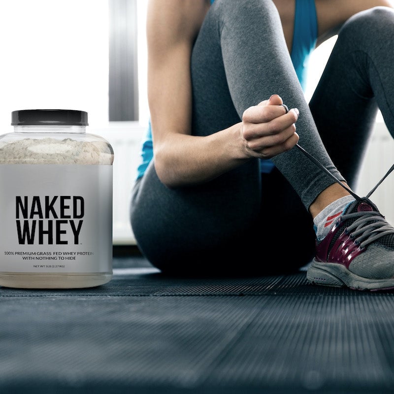 Tub of Naked Whey next to a woman tying her shoelaces in a gym