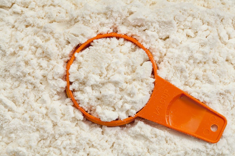 Cuchara de plástico naranja llena de proteína en polvo en un recipiente de proteína en polvo